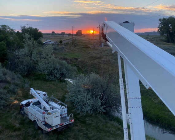 Photo from bucket truck raised above another bucket truck, facing a colorful sunset